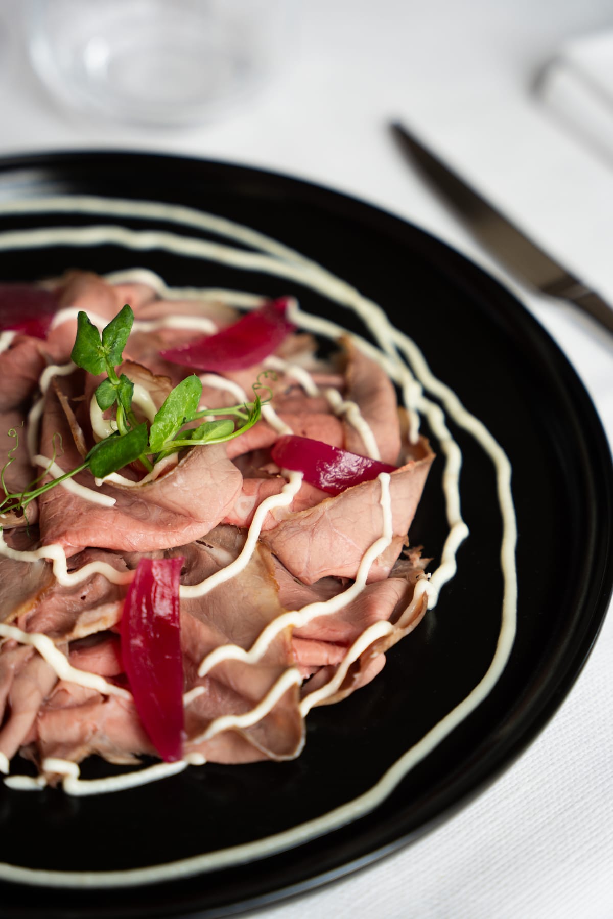 Carne a fette sottili con salsa a filo e germogli su piatto nero